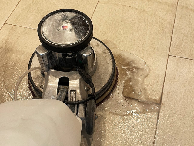 A floor machine is scrubbing away dirt and grime from a tile and grout floor.