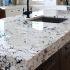 Quartz kitchen island countertop with white and black veining, undermount sink and faucet, dark wood cabinets below
