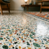 Low-angle view of a terrazzo floor with colorful chip patterns in green, orange, black, and white, in a living room setting with mid-century furniture.